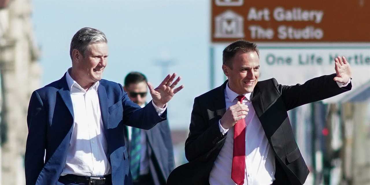 Keir Starmer and Paul Williams wave as they walk down the street.