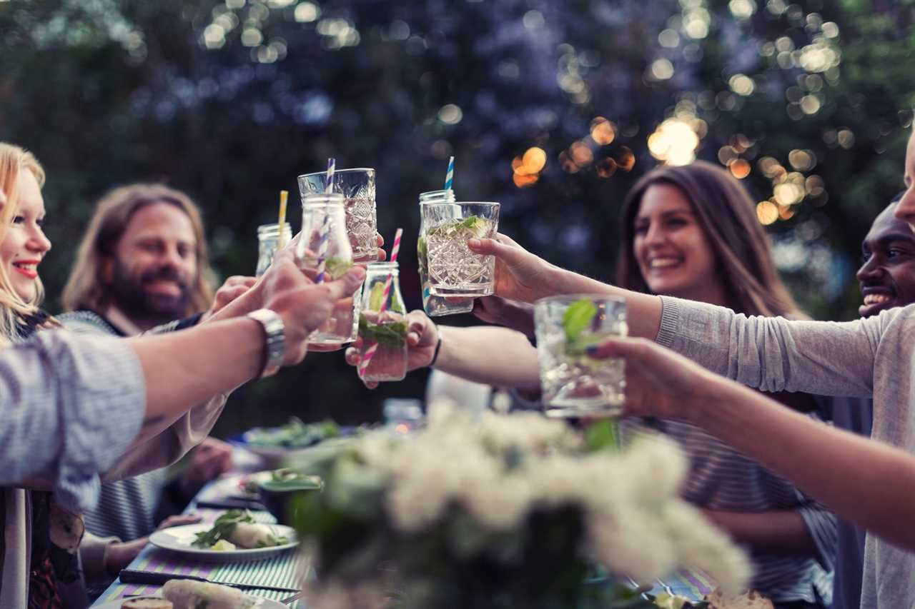 Friends sit around a table outside and cheers their glasses.