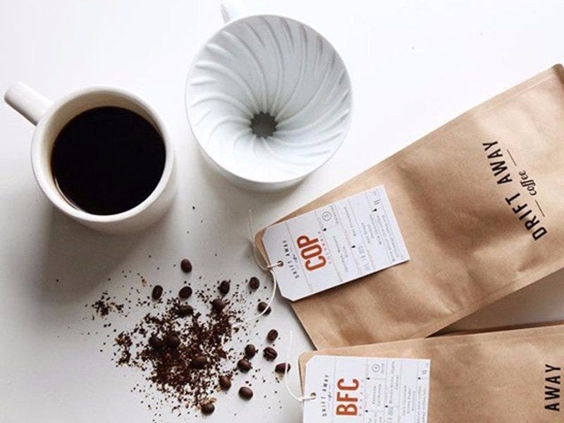 coffee grounds from Driftaway spill out of a brown bag onto a table with a cup of coffee and a pour over brewer as part of the best coffee subscription service in 2021