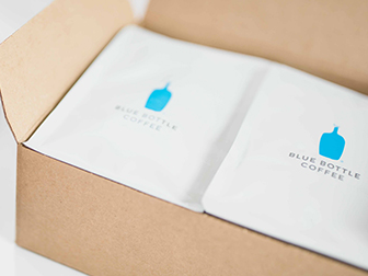 A box containing bags of Blue Bottle coffee sits open next to two cups of coffee as part of the best coffee subscription boxes in 2021