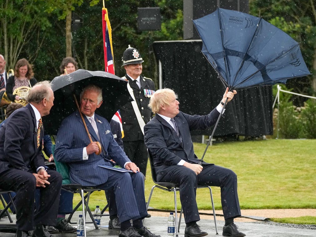 Prince Charles, Prince of Wales looks concerned as British Prime Minister, Boris Johnson's umbrella is blown inside-out at The National Memorial Arboretum on July 28, 2021 in Stafford, England.