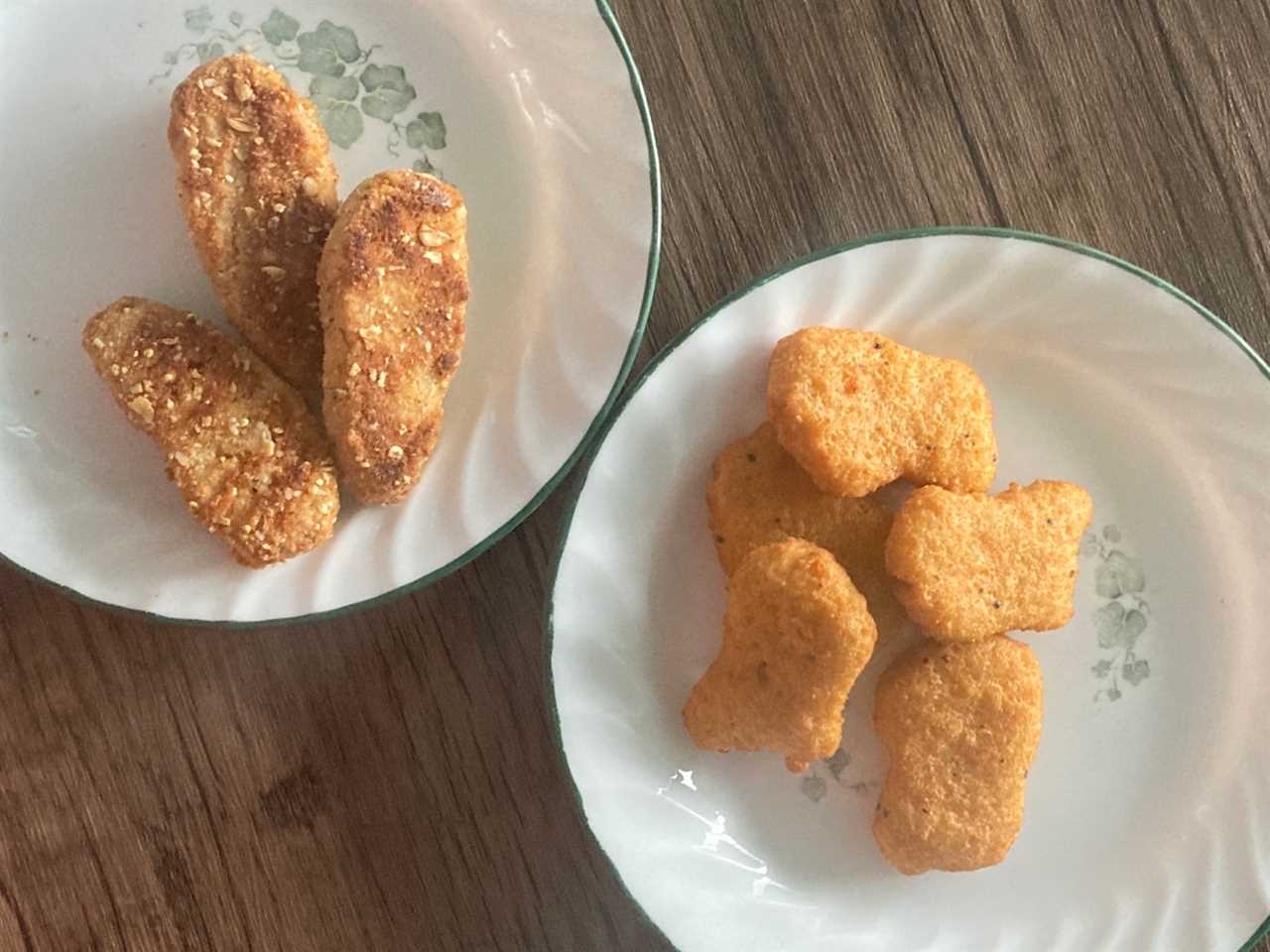 Two white plates with two kinds of vegan chicken nuggets on a wooden table