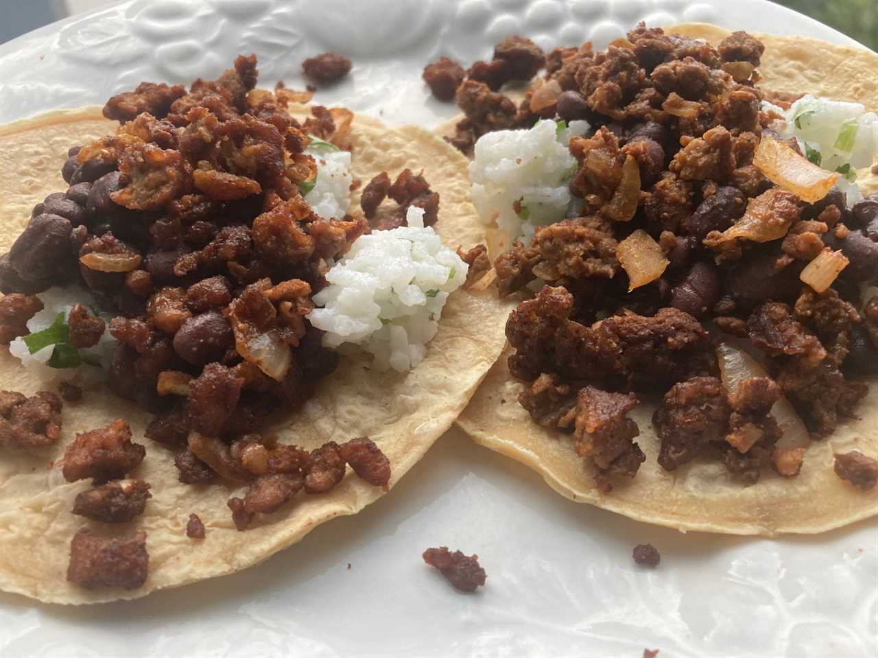 An image of two tacos on a white plate with beans, rice, and two different types of meatless ground beef