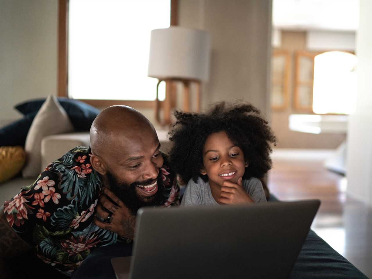A father and daughter watch TV on a laptop together