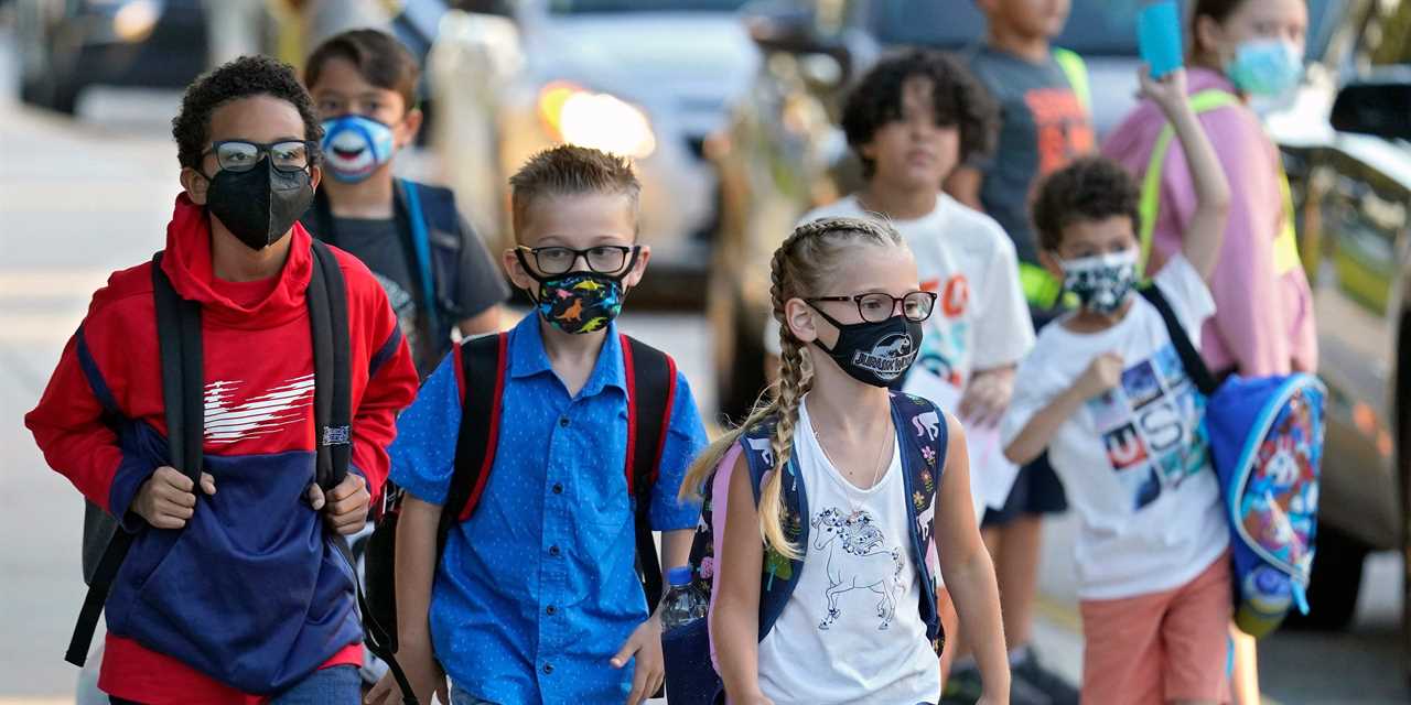 School children walk with masks and backpacks on.
