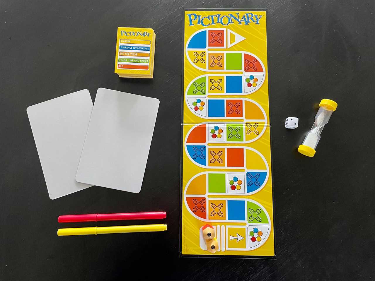 Image of the Pictionary board game laid out with cards, a dice, a timer, and pens to the side, best board games 2021