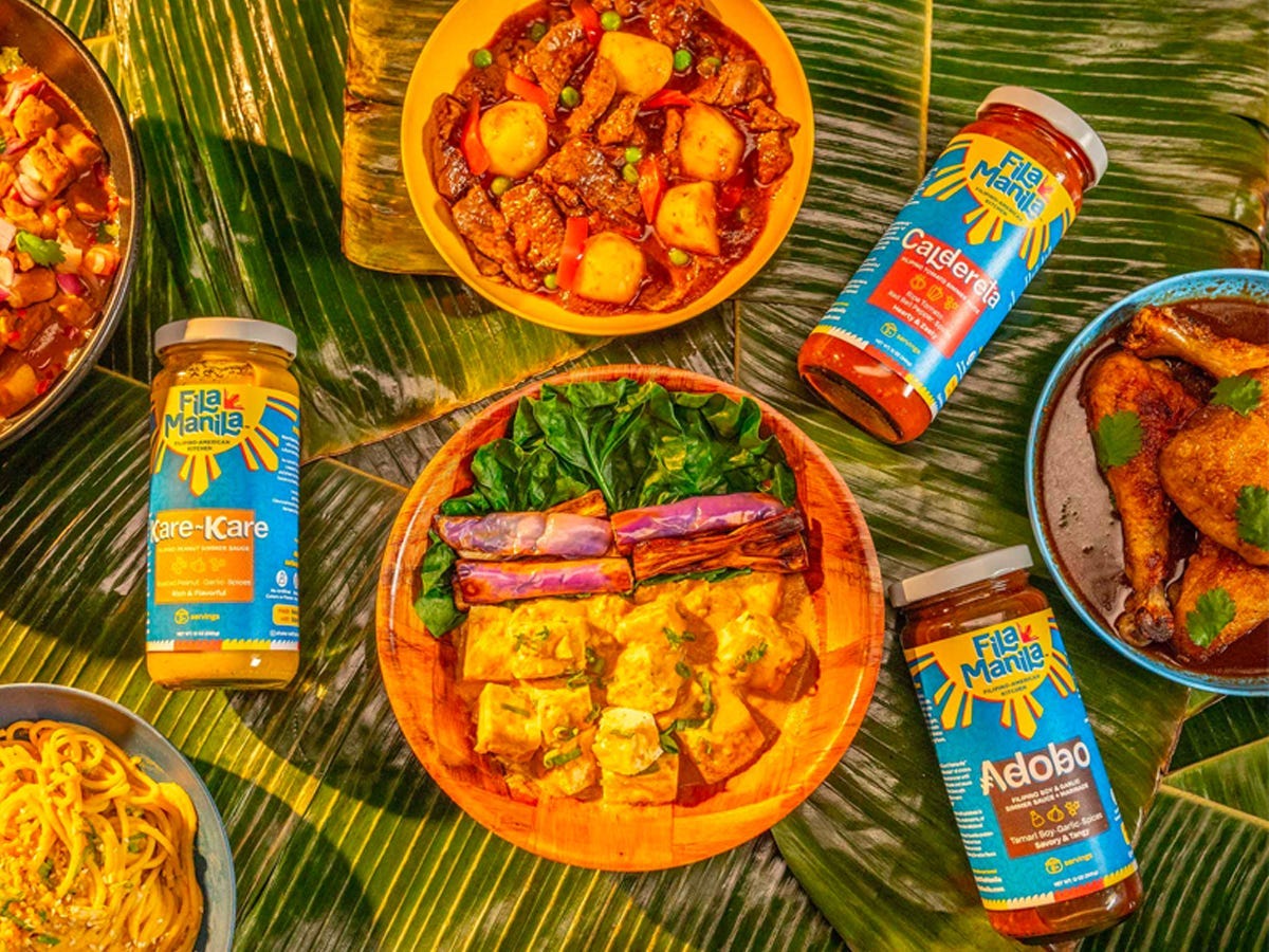 Simmer sauces from Fila Manila alongside Filipino dishes on top of table of banana leaves - Best Asian American food and drink brands in 2021