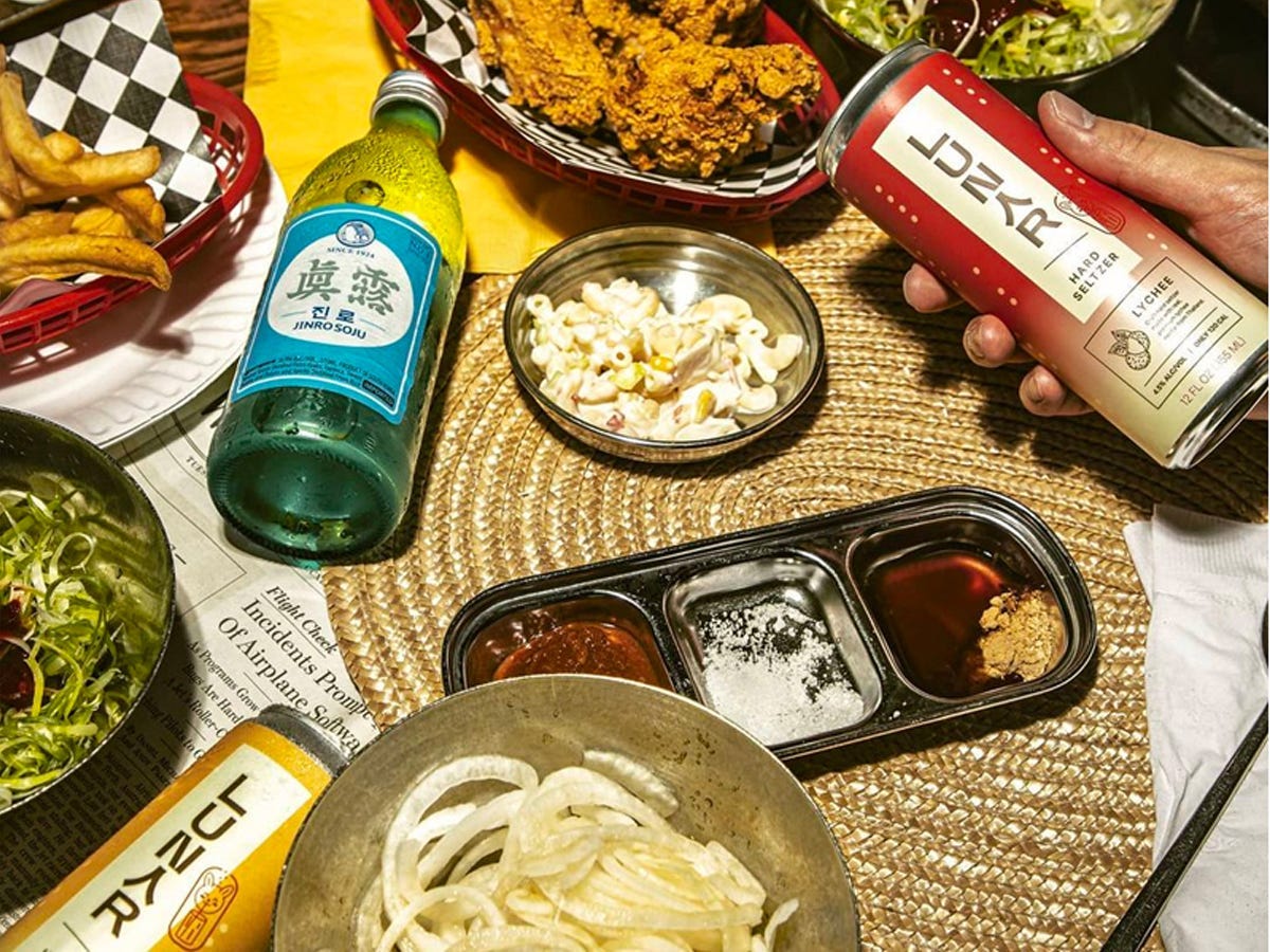 Table spread of Korean fried chicken, fries and snacks alongside hands holding cans of Lunar hard seltzer - Best Asian American food and drink brands in 2021