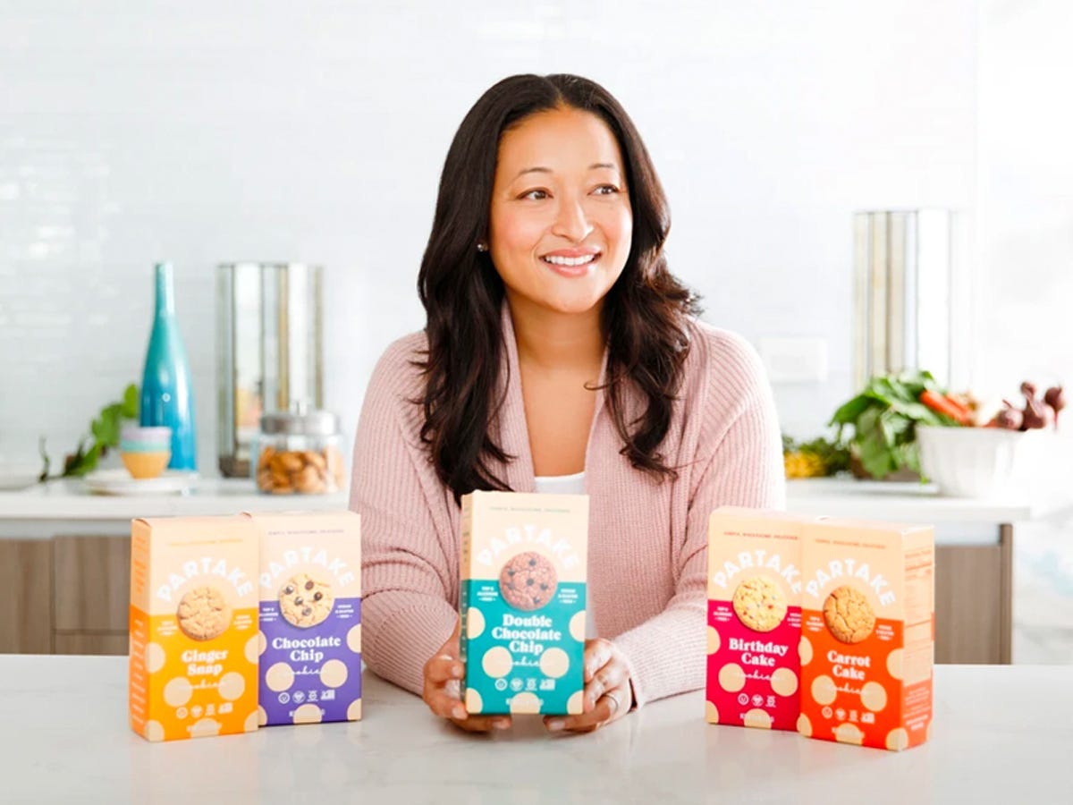 Woman at kitchen counter holding boxes of Partake Foods cookies - Best Asian American food and drink brands