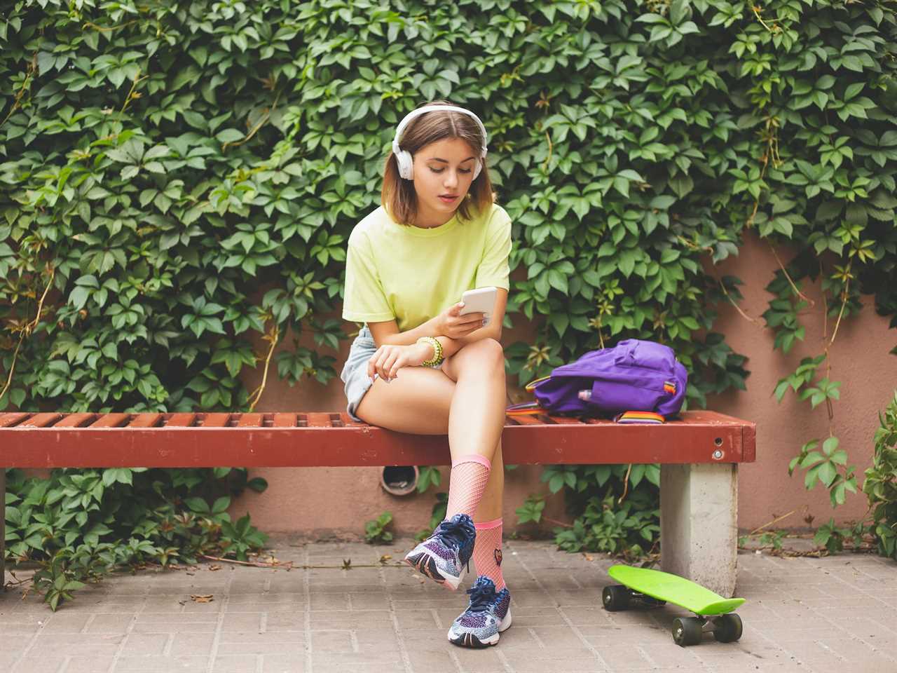 Teen skateboarder using phone with headphones outside