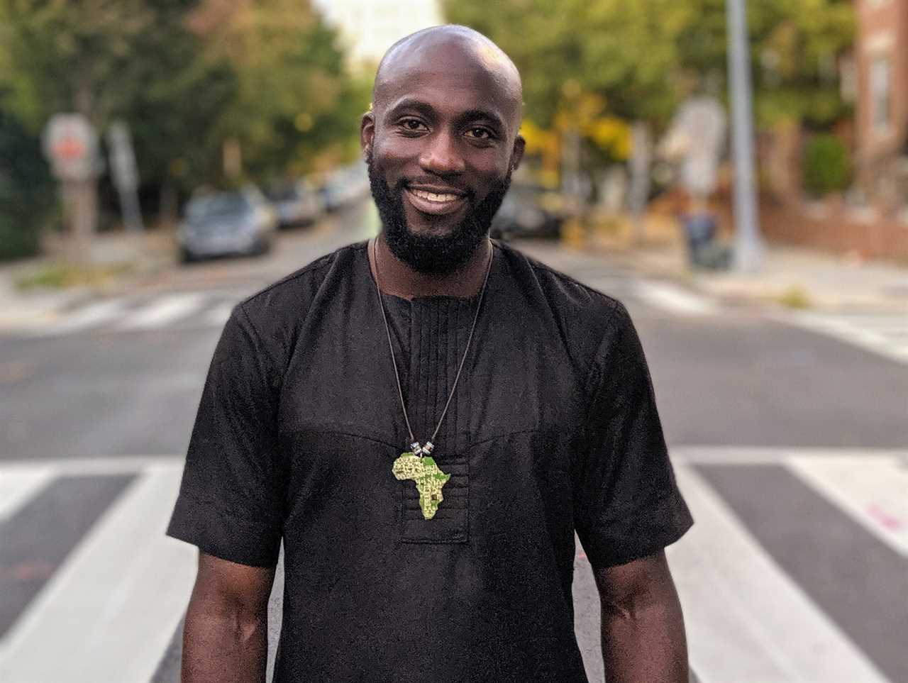 Oladosu Teyibo stands wearing a black shirt in the middle of the street smiling