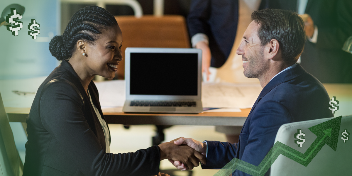 Two people shaking hands and smiling while sitting in front of a laptop at an office.