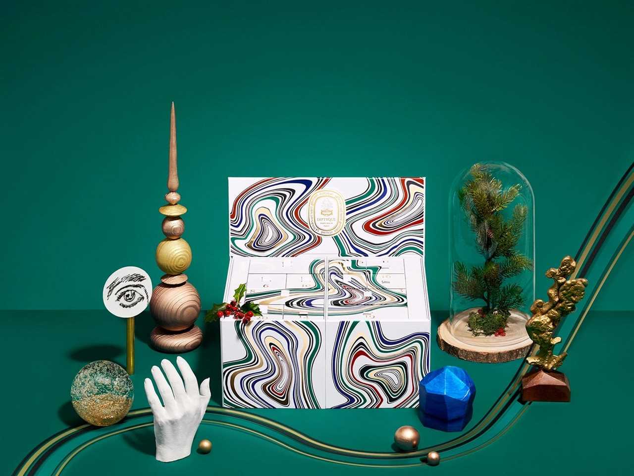 Image of Diptyque advent calendar surrounded by knick knacks on a green background for best advent calendars 2021