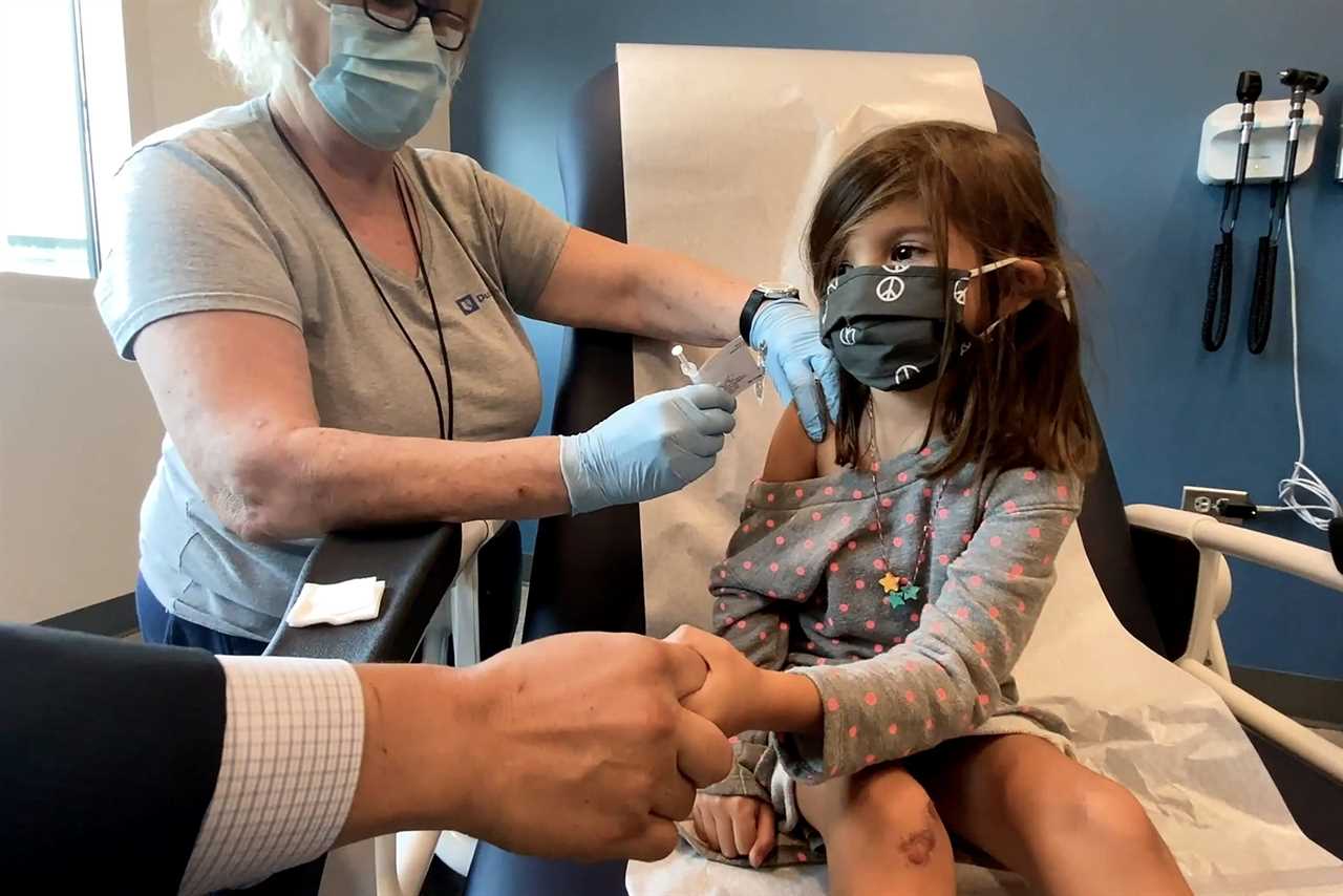 Bridgette Melo, 5, holds the hand of her father, Jim Melo, during her inoculation of one of two reduced 10 ug doses of the Pfizer BioNtech COVID-19 vaccine during a trial at Duke University in Durham, North Carolina September 28, 2021 in a still image from video. Video taken September 28, 2021.