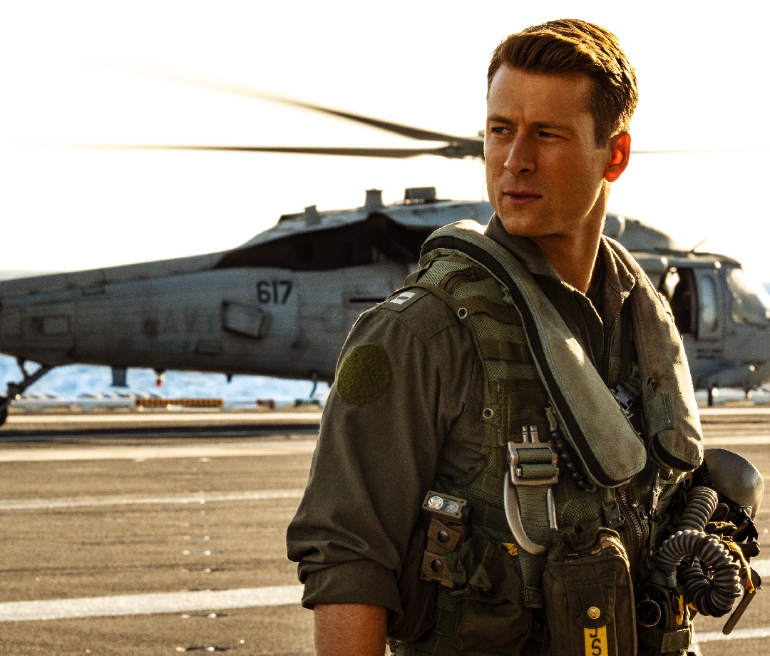 Actor Glen Powell stands in front of a helicopter on a naval base during the filming of Top Gun: Maverick.