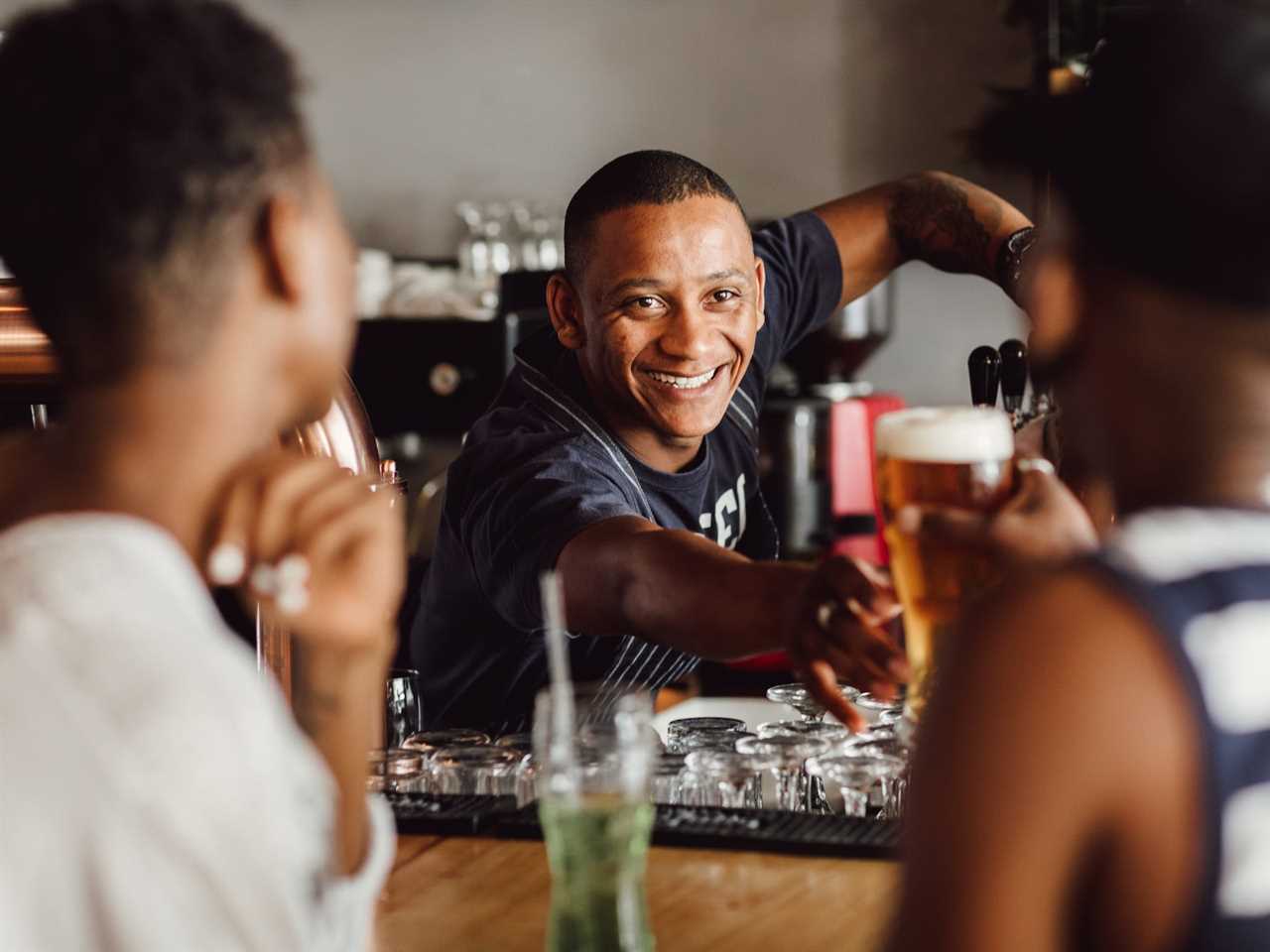 A bartender reaching to give or take beer from customers who are out of focus in the foreground