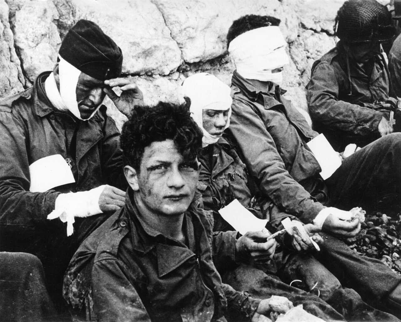 A group of U.S. wounded soldiers sheltering behind a wall after the Normandy landing at Omaha Beach