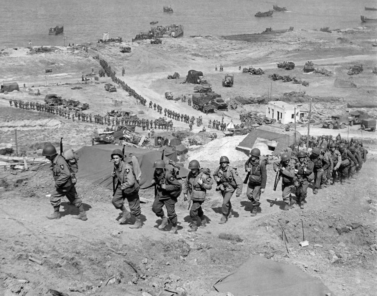With ships and supply vehicles below them, American troops march up from Omaha Beach during the invasion of Normandy, Normandy, France, June 18, 1944.