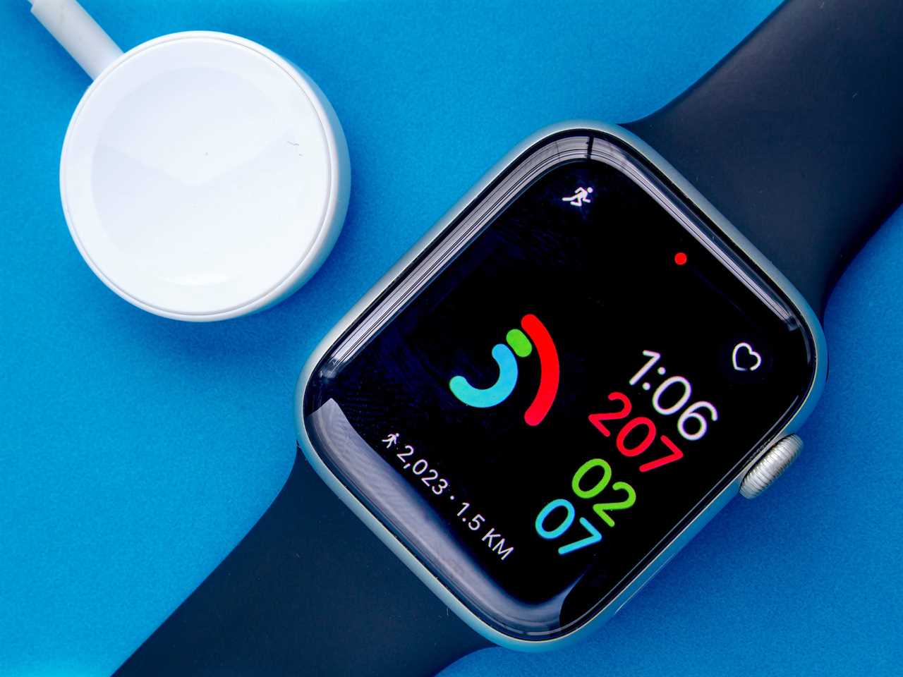 An Apple Watch and Apple Watch charger laying on a blue background.