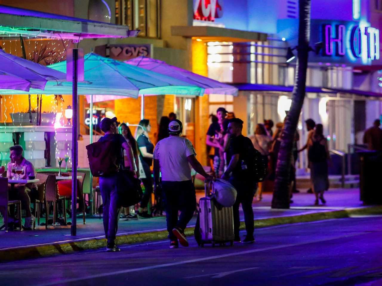 Spring breakers walk down a street at night in Miami.