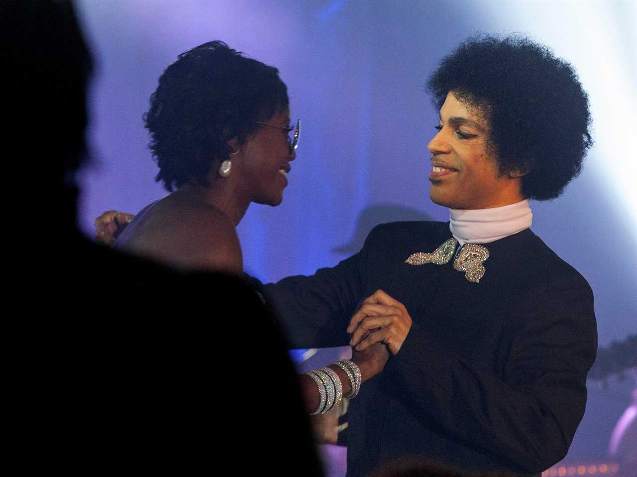 Mellody Hobson holds hands and smiles with Prince onstage