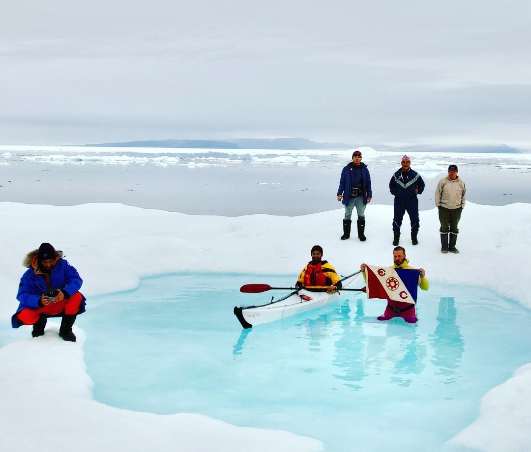 Group of men standing around swimmer and kayaker in Arctic water