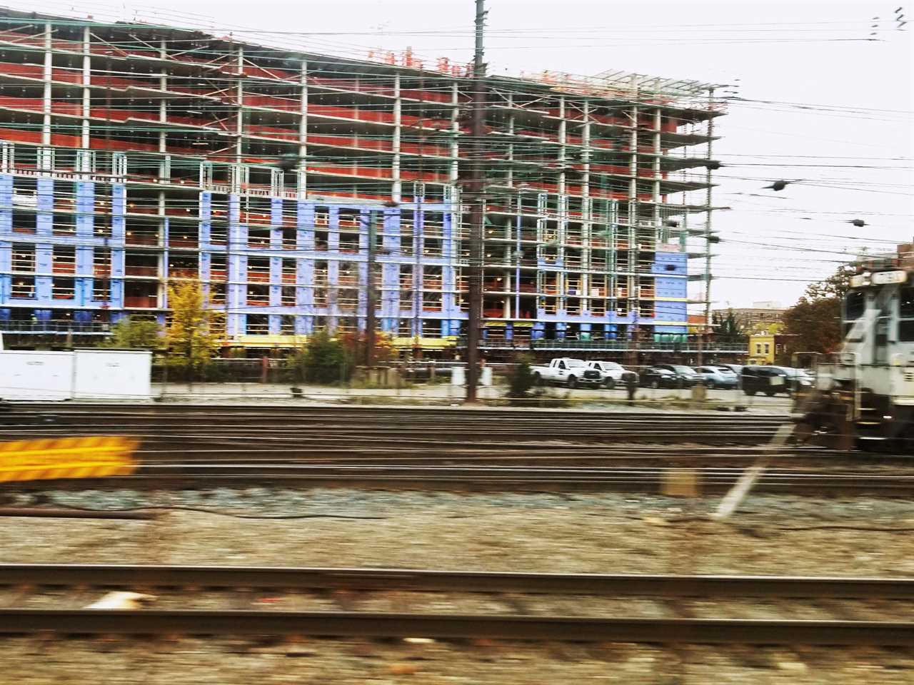 An apartment building under construction with train tracks running in front of the building.