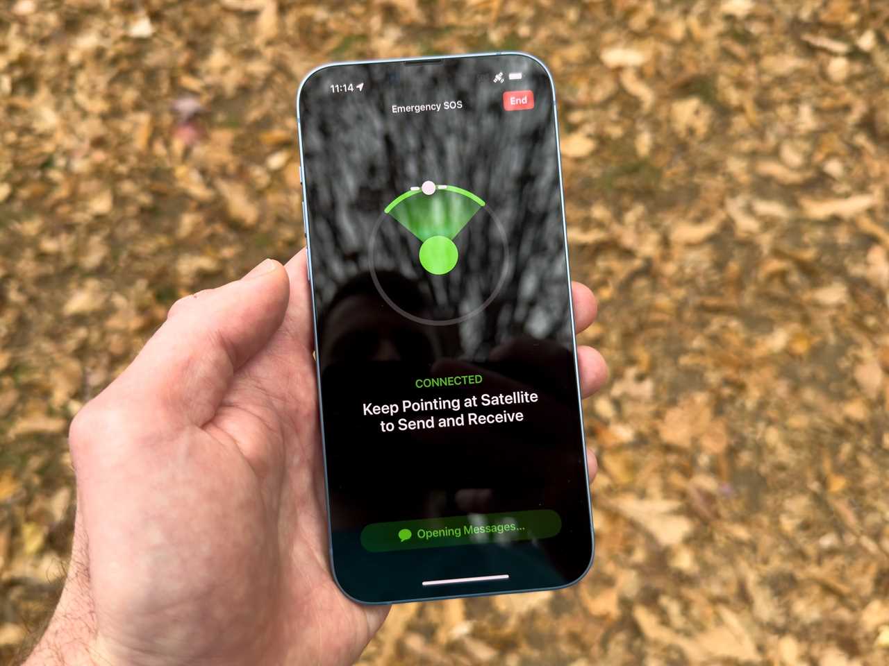 A hand holding an iPhone showing the Apple Emergency SOS via Satellite signal.