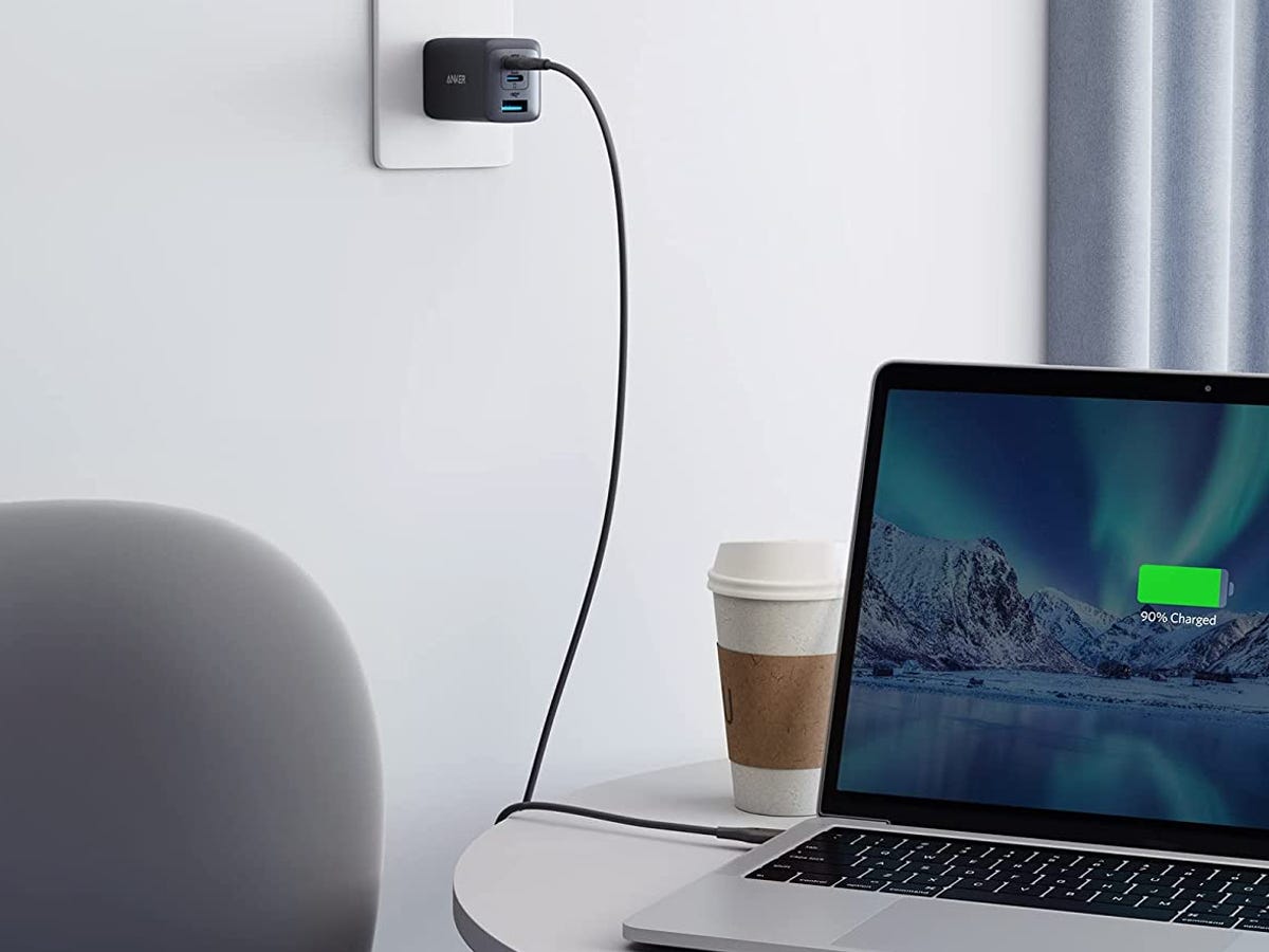 a Anker 735 Charger (Nano II 65W) is plugged into the wall charging a laptop next to a to-go coffee cup as one of the best tech products under $50