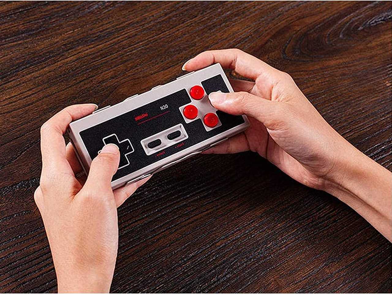 a person holds a 8bitdo N30 Gaming Controller, resting their wrists on a table as one of the best tech products under $50