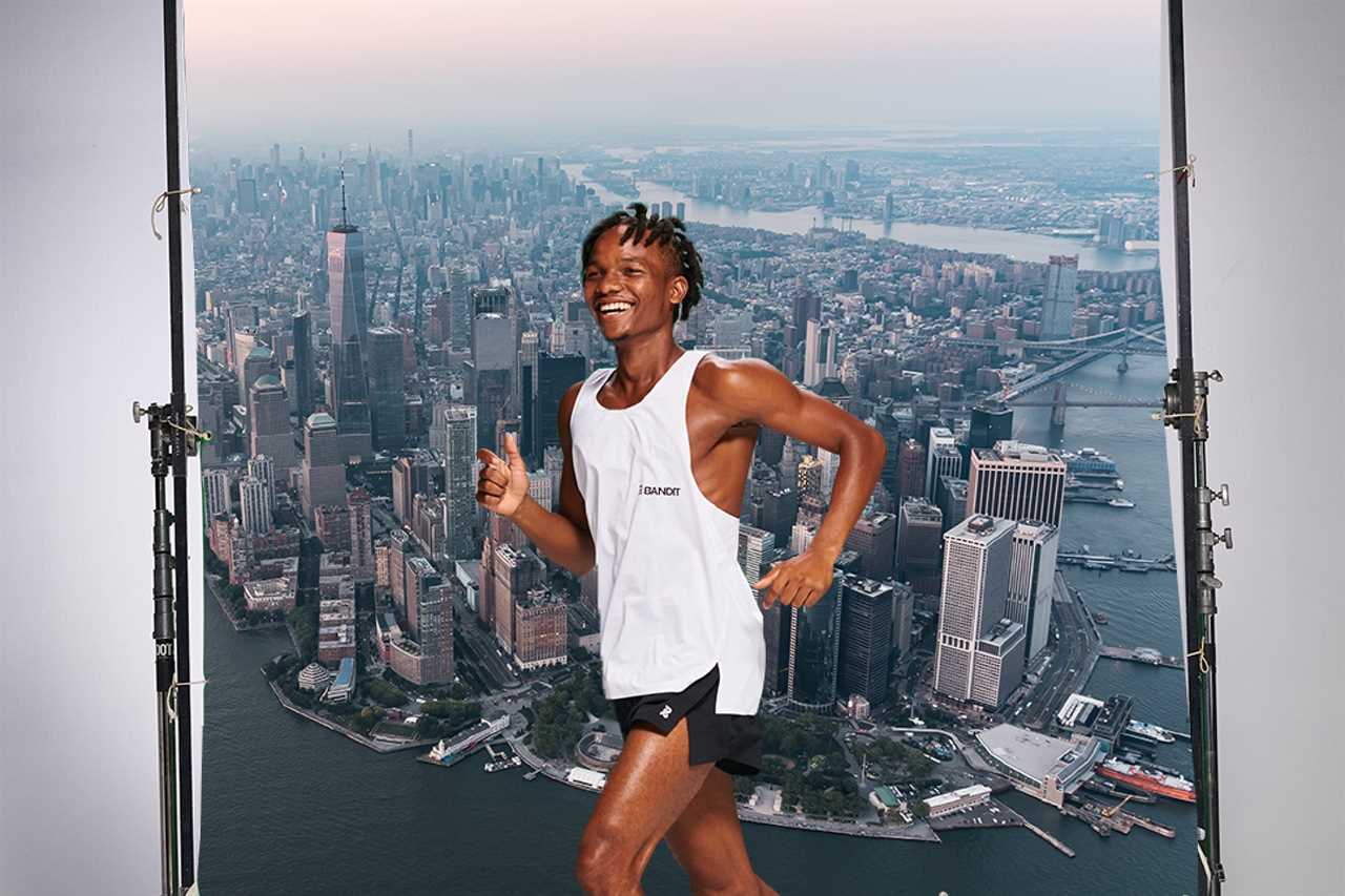 Black runner in white tank and black shorts posing in front of New York City skyline backdrop