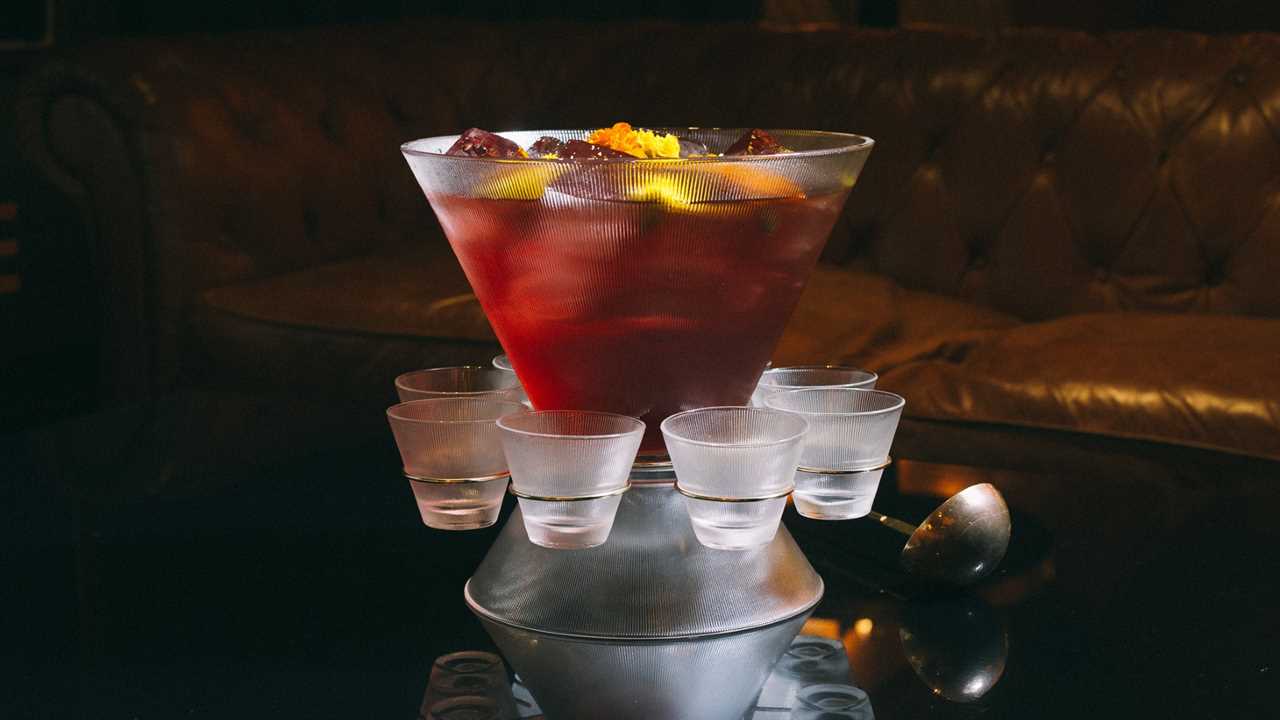 Large punch bowl filled with red drink and fruit encircled by empty shooter glasses.