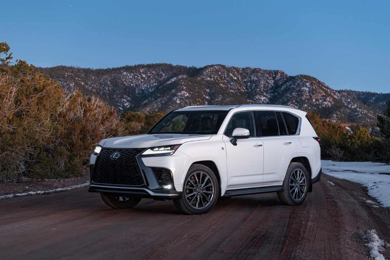 White luxury SUV on a dirt road with mountains in the background.