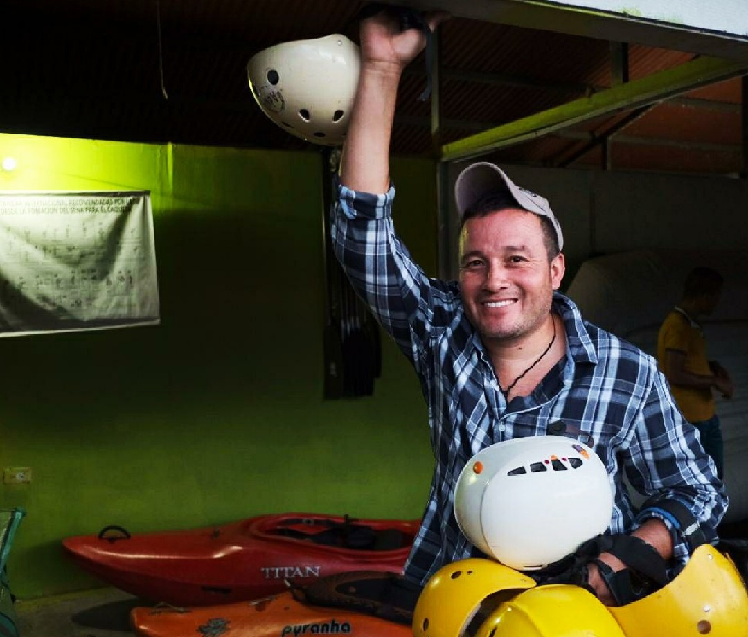 Frellin Alberto Noreña smiling with a pile of rafting helmets in hand.