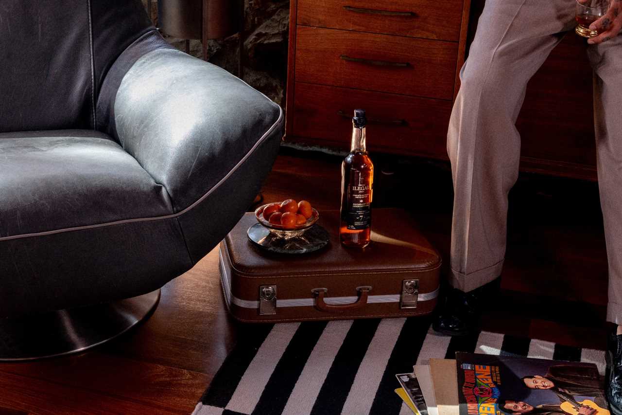 Bottle of Ilegal Mezcal 7-Year Añejo on table with leather chair to its left and black-and-white striped carpet underneath