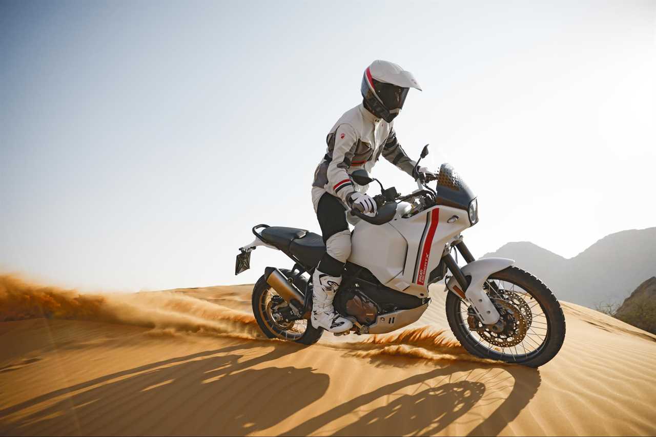 Man riding an adventure motorcycle through a sand dune in the daytime.