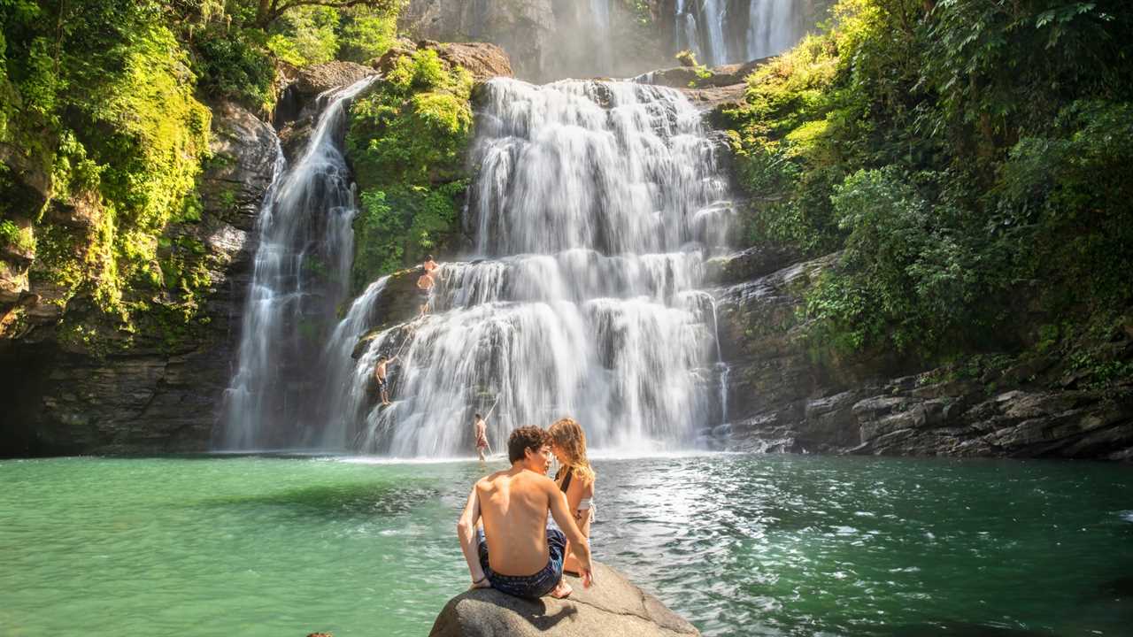 Young people enjoy swimming in a waterfall in the jungle