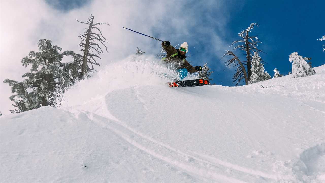 Man skiing on backcountry skis across a steep snowy slope with pine trees in the background.