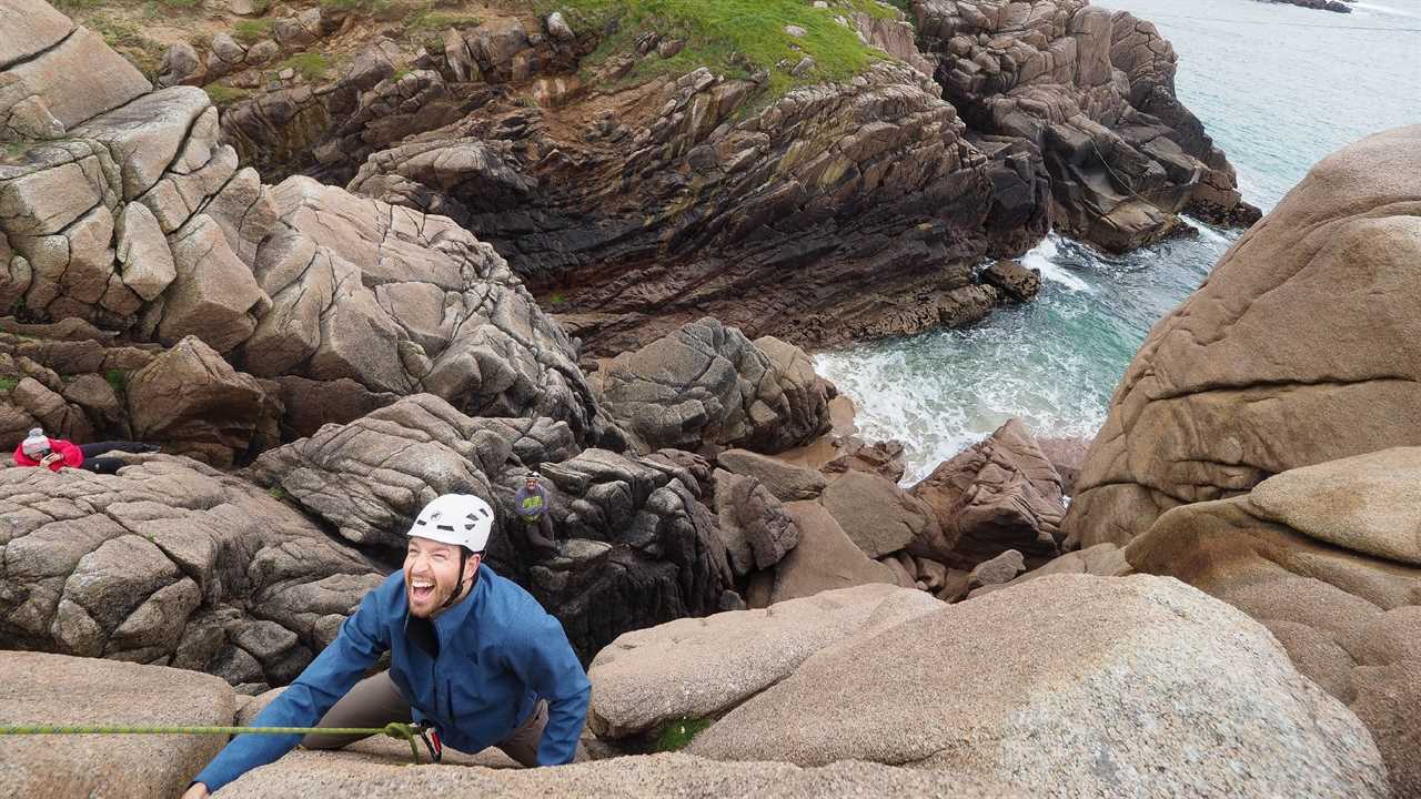 Man in helmet climbing a coastal cliff in Ireland.