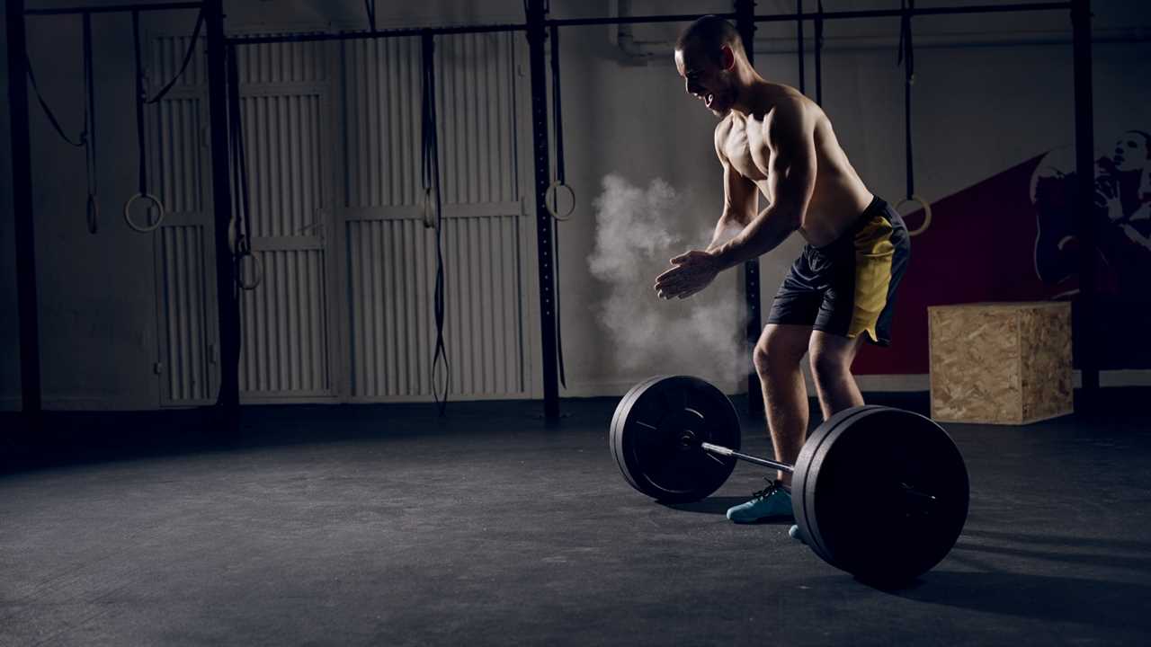 Man in a gym clapping his hands with powder over a barbell. muscle-building exercises