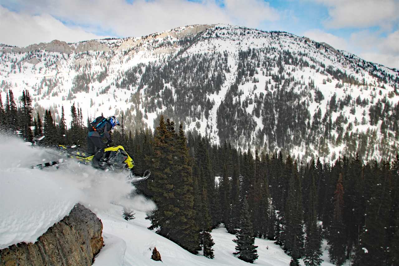 Man riding a snowmobile off a mountainside.