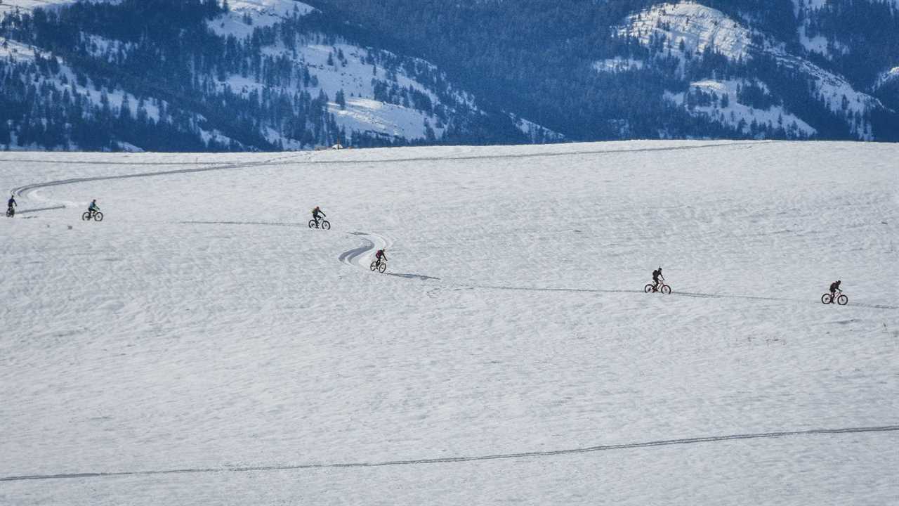 Fat bikers wind single file along a snowy trail with a mountain backdrop in northeastern WA's Methow Valley