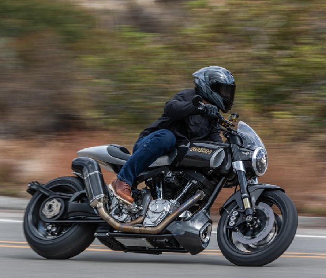 Man riding an Arch 1s sport cruiser motorcycle on a road with a blurred background.