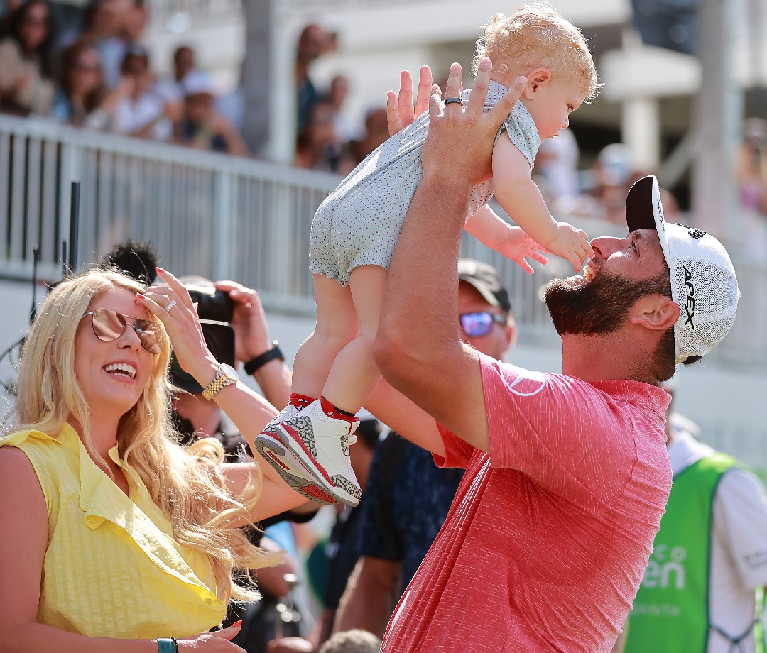 Jon Rahm holding his baby in the air next to his wife.