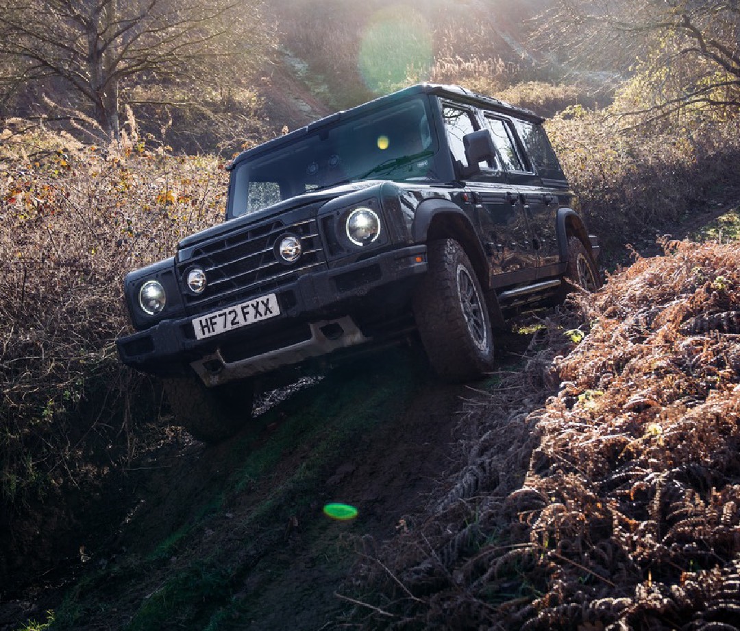 Boxy green 4x4 SUV scrambling up a muddy hill.