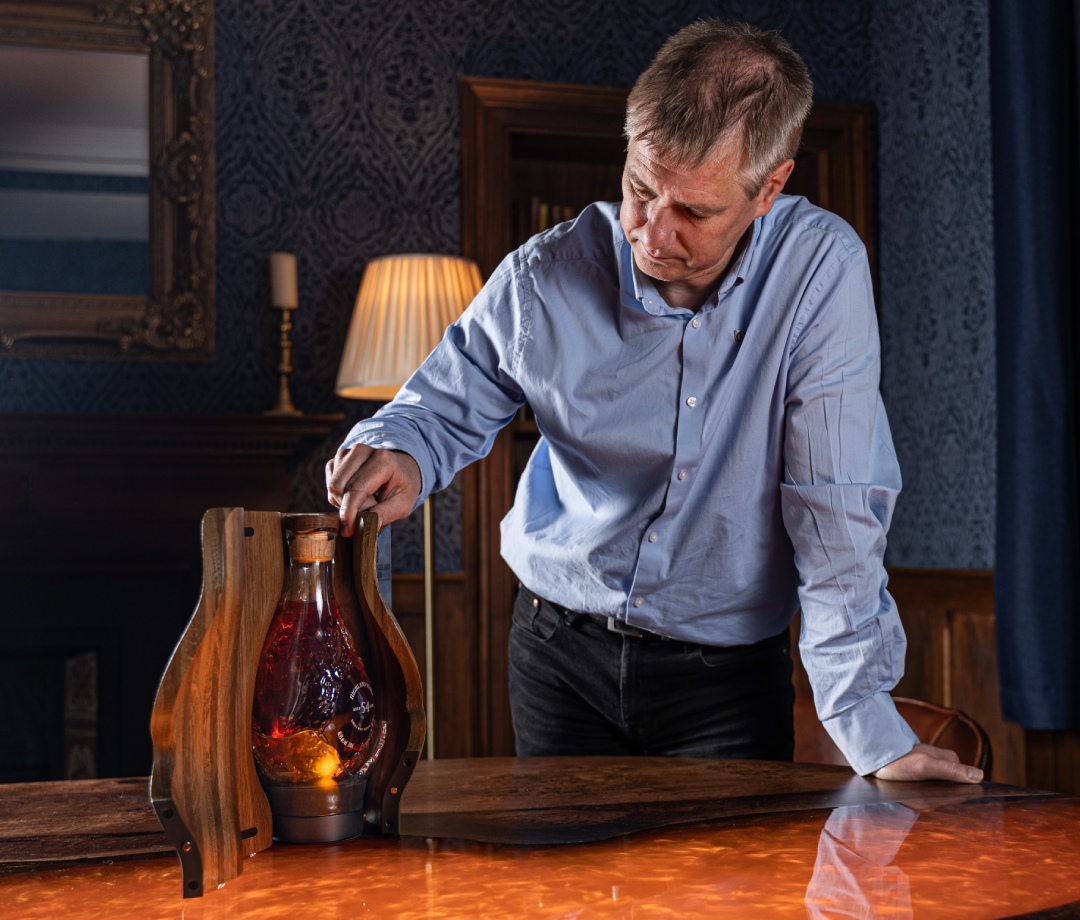 Mature caucasian man wearing blue dress shirt admiring whiskey in bespoke wooden box