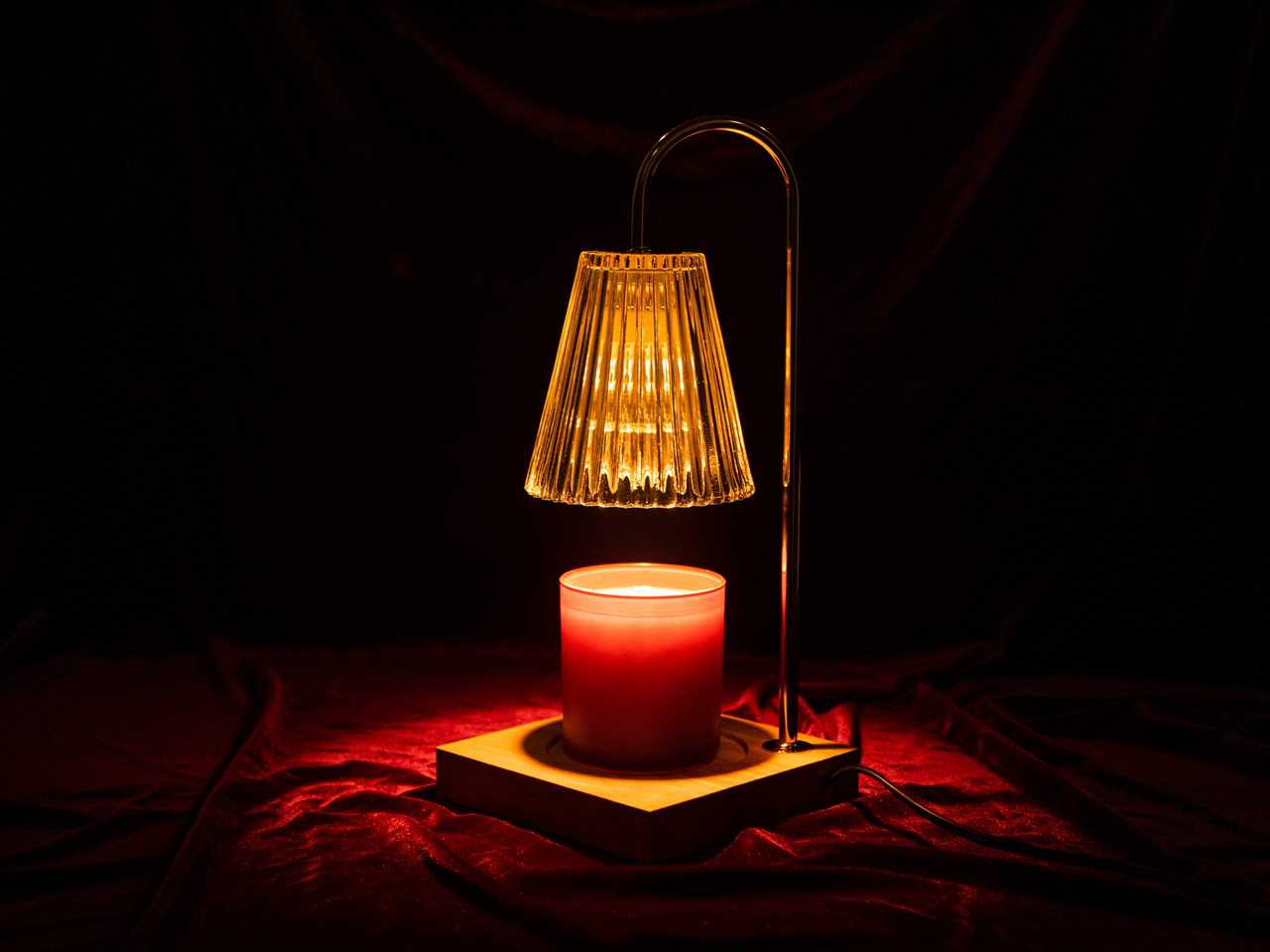 a luzdiosa Candle Warmer Lamp warms a candle in a dark room with a red velvet surface underneath