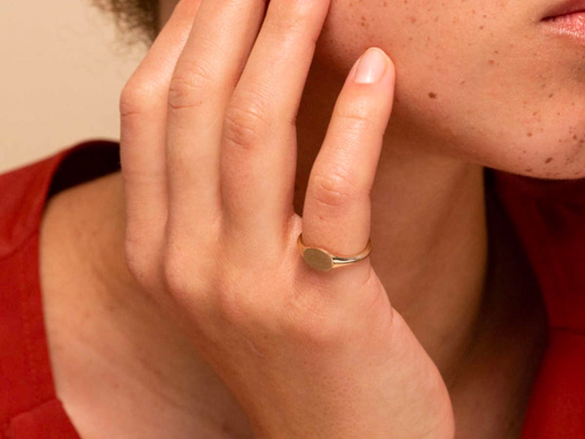 Person holding a hand to their chin modeling a gold Signet ring on their pinky finger.