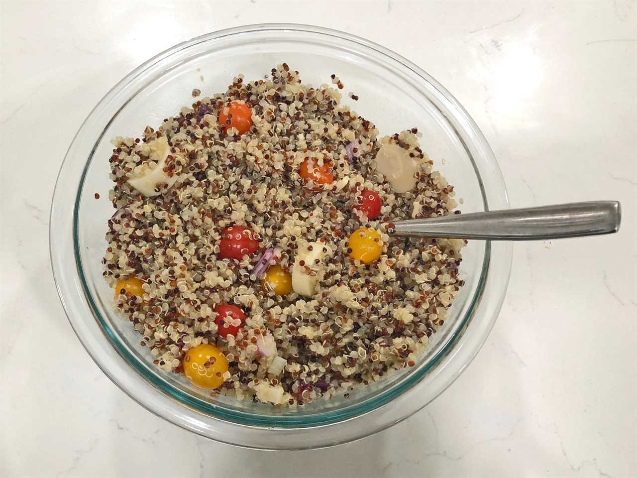 A clear bowl filled with quinoa salad, made with sliced red onions, hearts of palm, cherry tomatoes, and cooked quinoa.