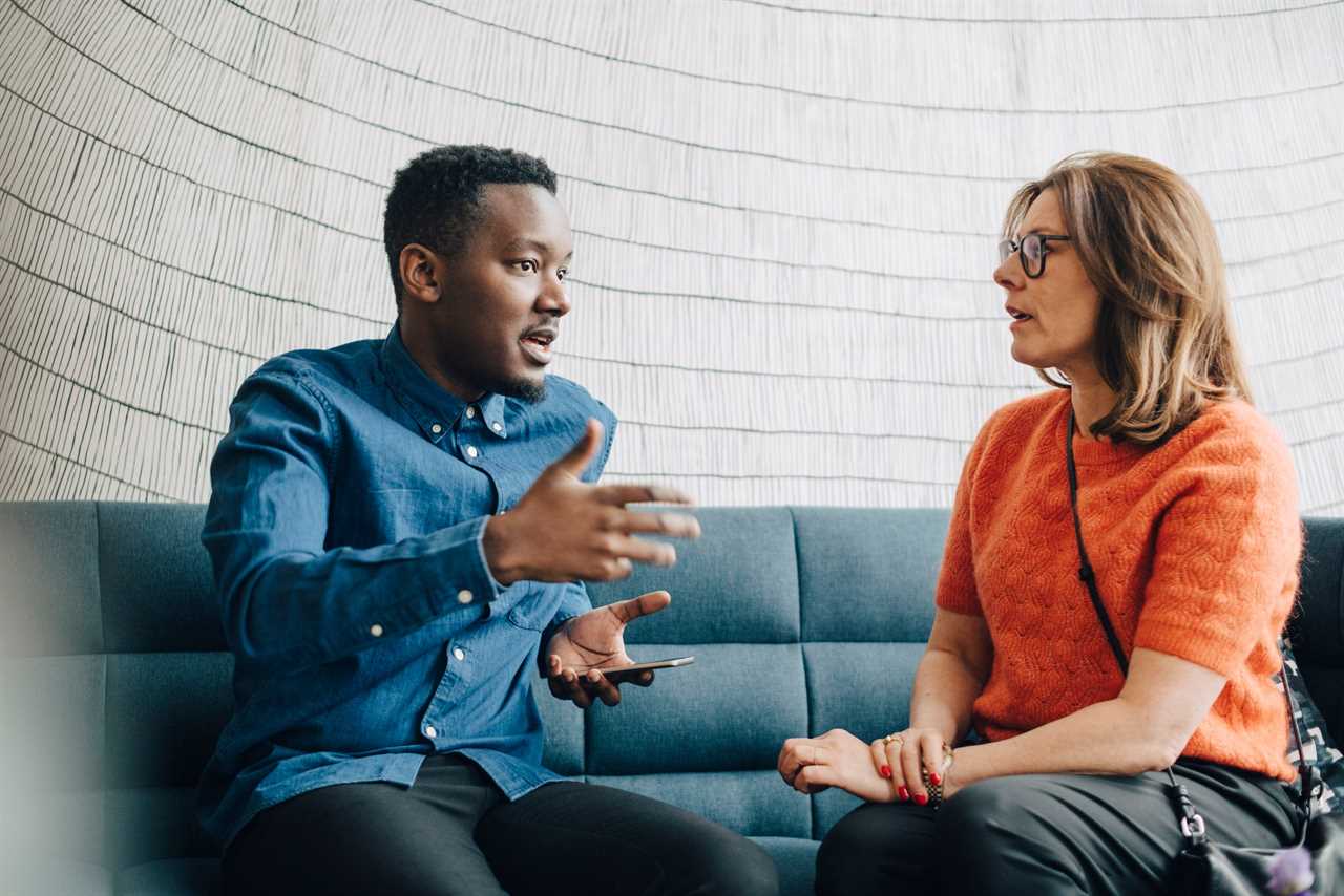 Two colleagues talking while sitting on a couch in a conference room.